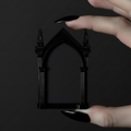 Hand holding a small black arch-shaped picture frame against a dark background