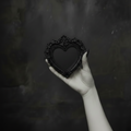 Hand holding a black heart-shaped frame against a dark background.
