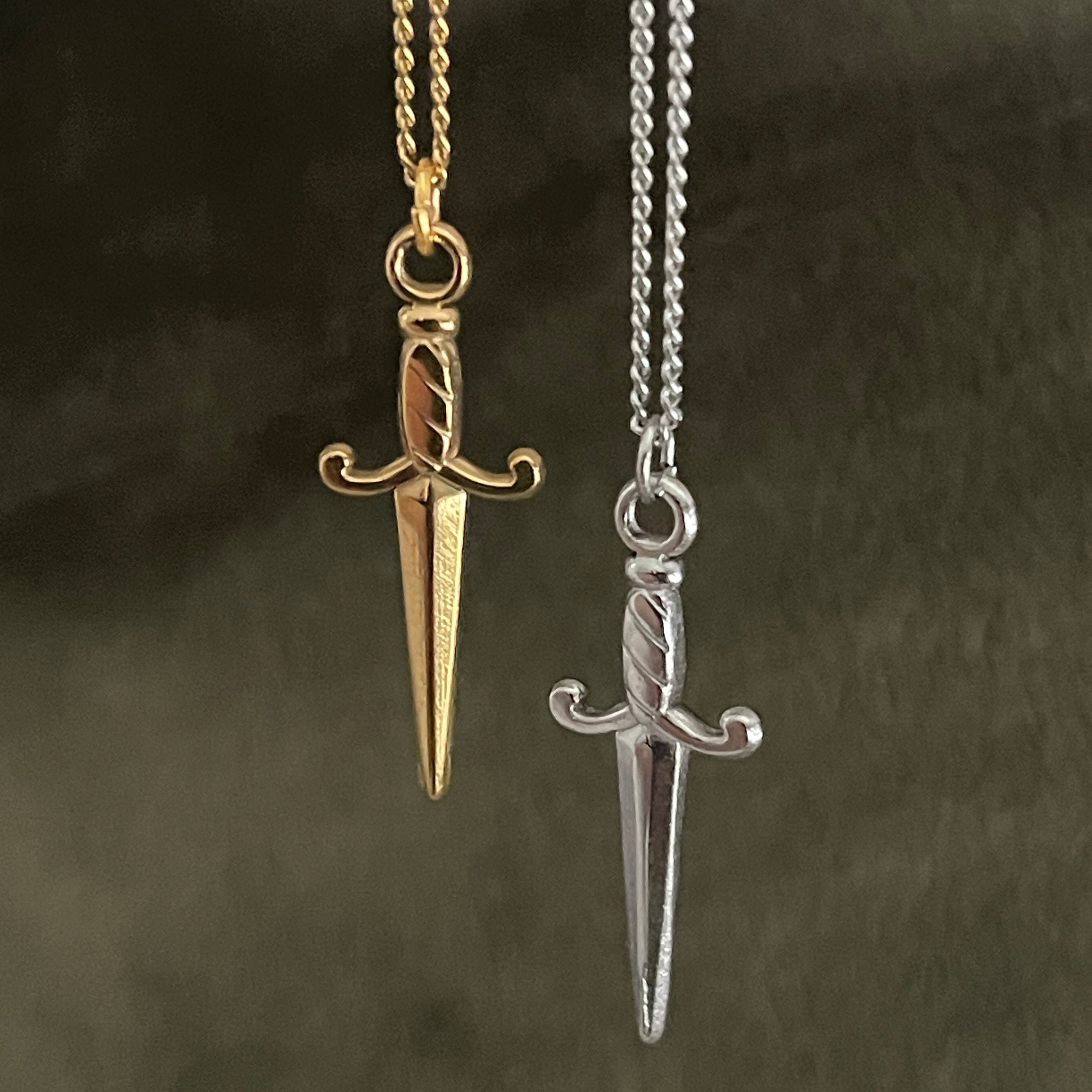 Gold and silver dagger-shaped pendants on chains against a dark background