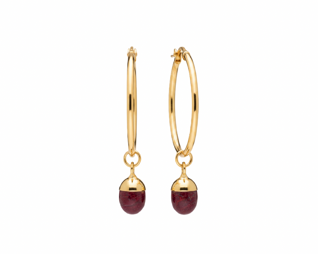 A pair of gold hoop earrings with small oval dark pink gemstone drops, shown on a plain white background.