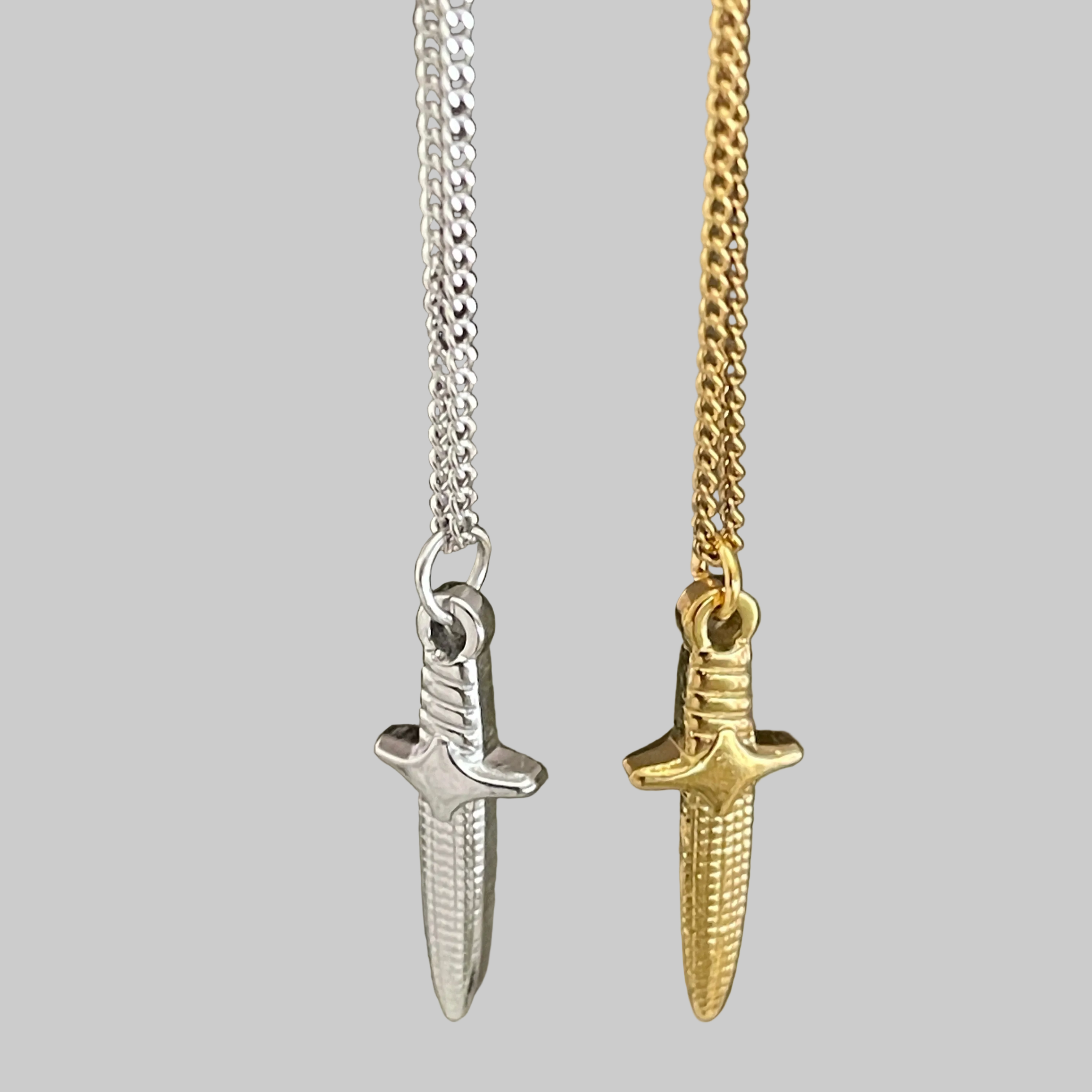 Two sword-shaped pendants on chains against a gray background