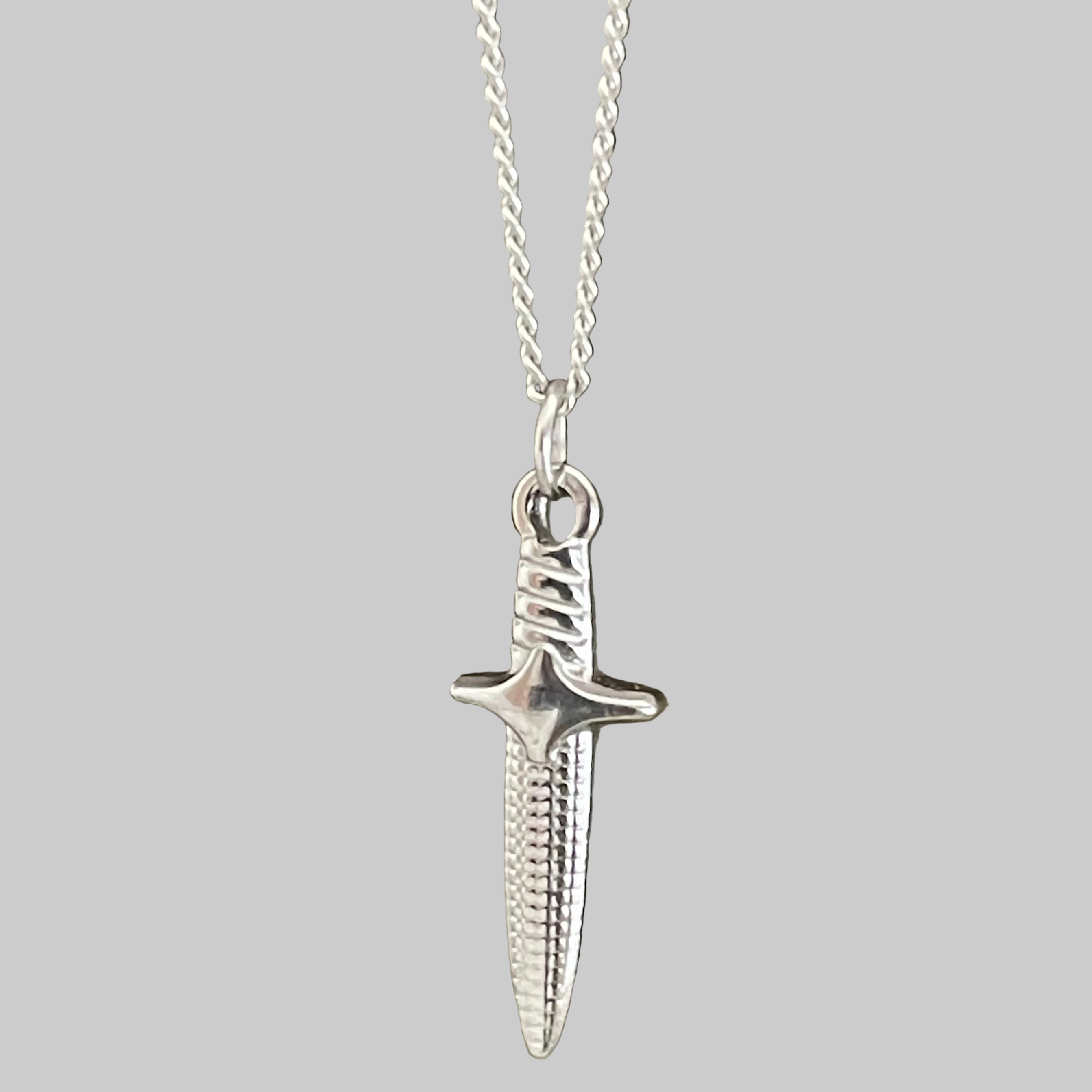 Silver dagger pendant on a chain against a gray background