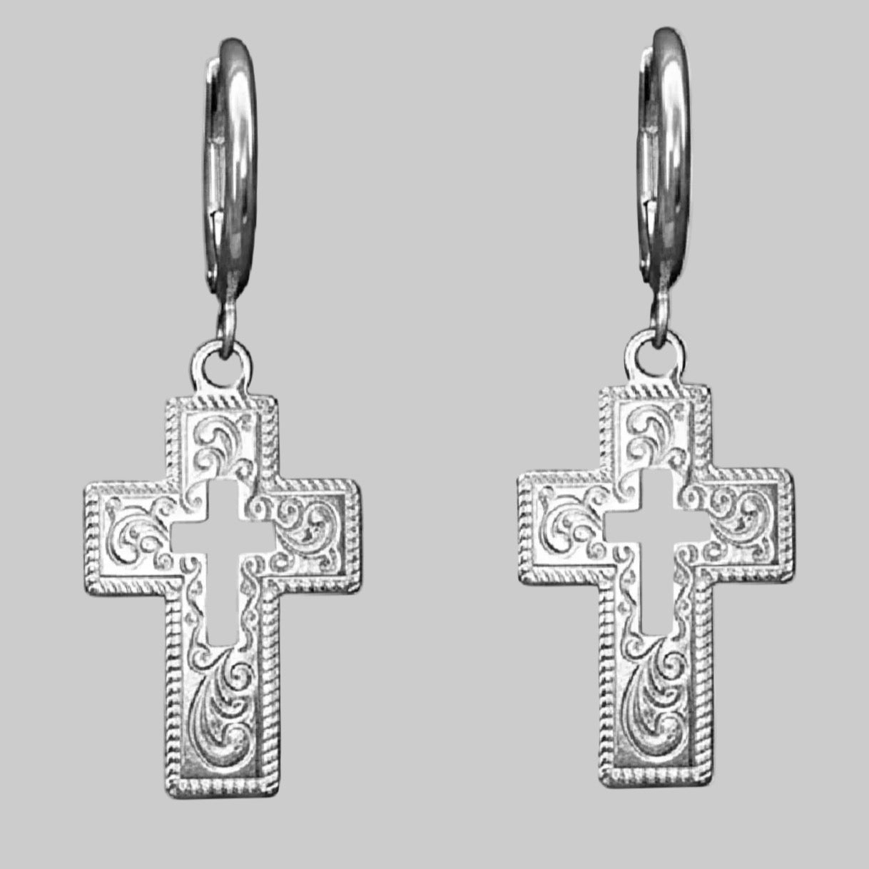 Silver crss earrngs on a light grey background.