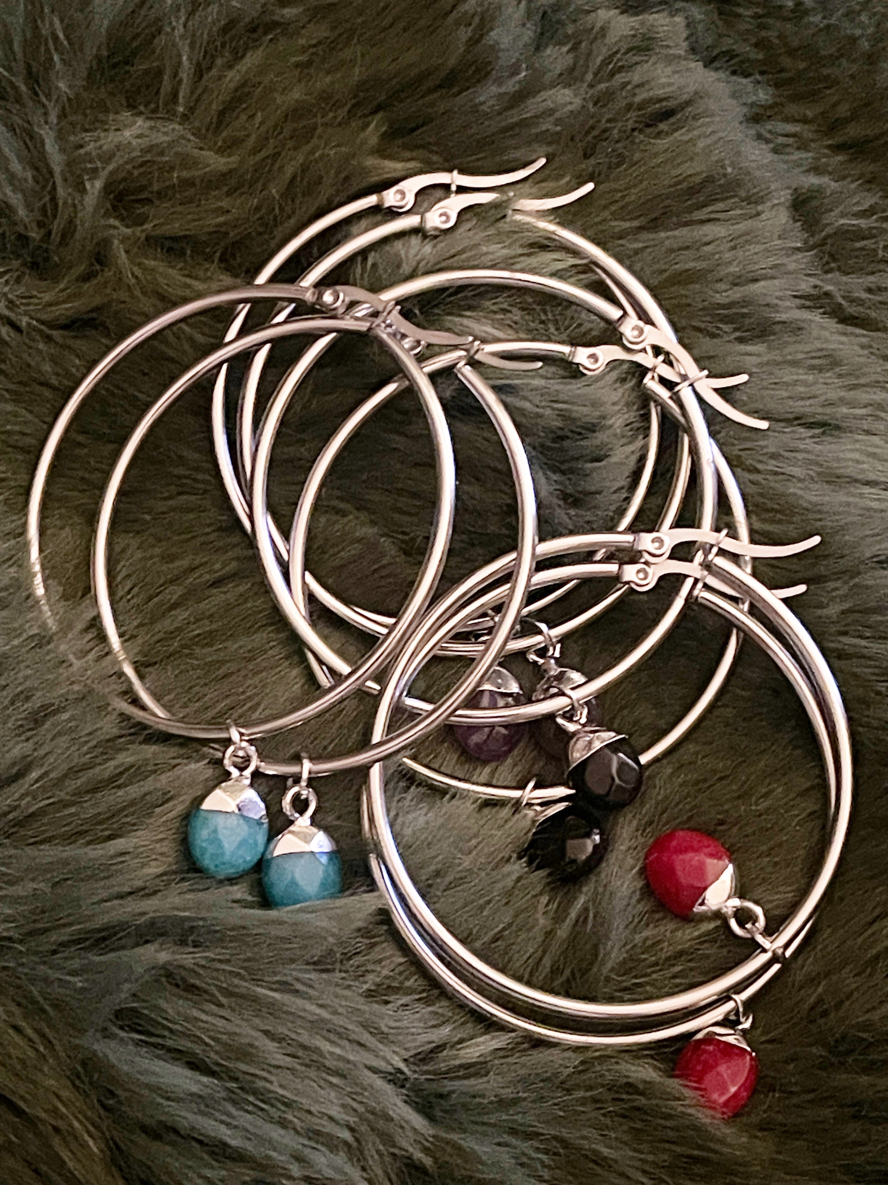 Set of silver bangles with colourful gemstone charms on a fur surface