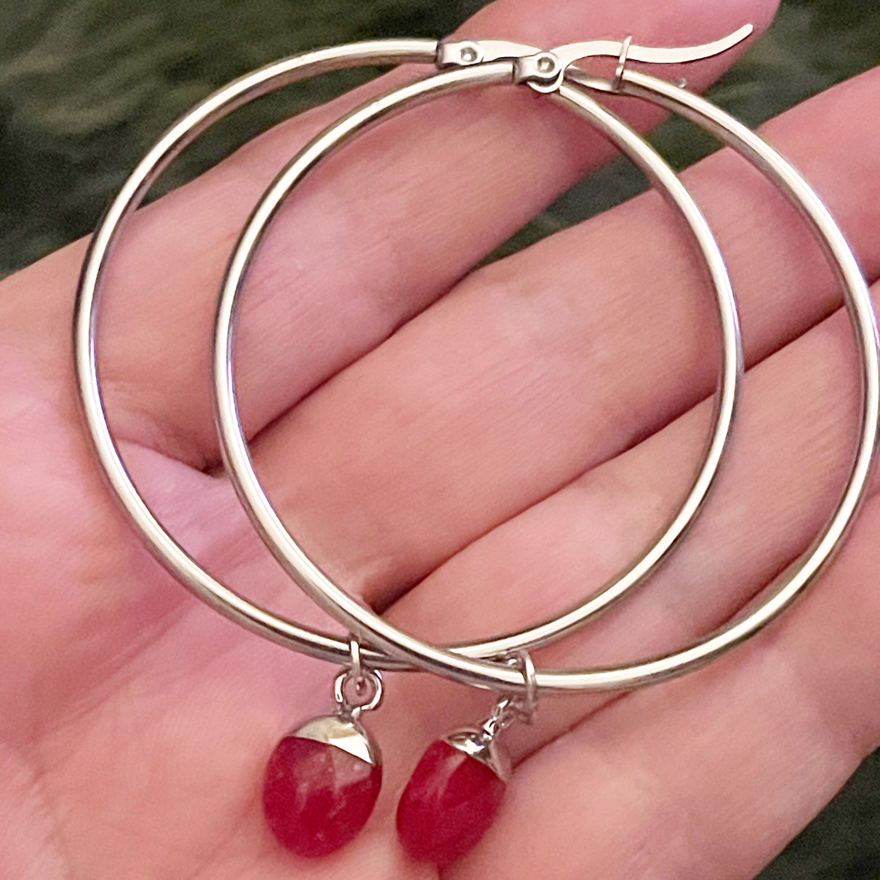 Silver hoop earrings with red gemstone drops held in a hand.