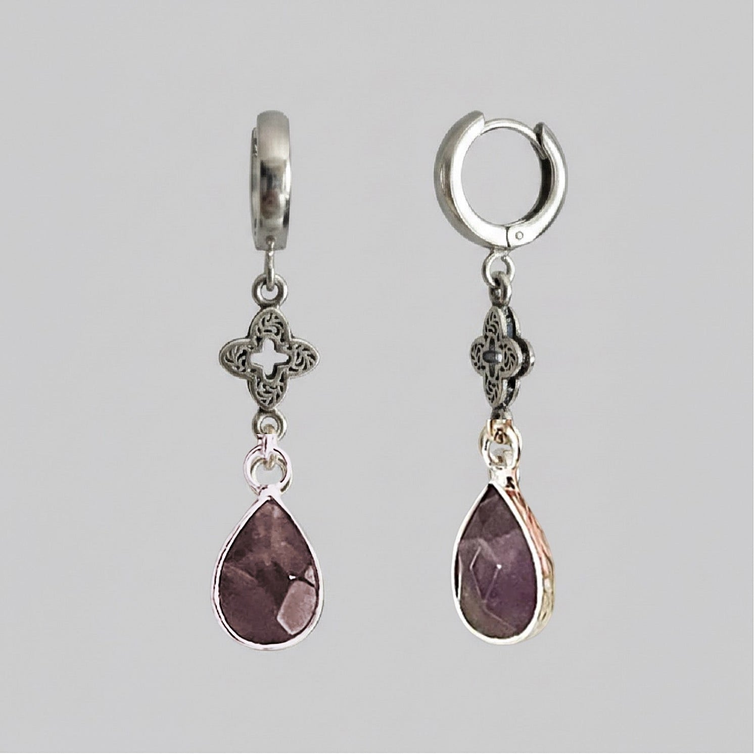 Pair of silver earrings with purple teardrop-shaped stones on a gray background