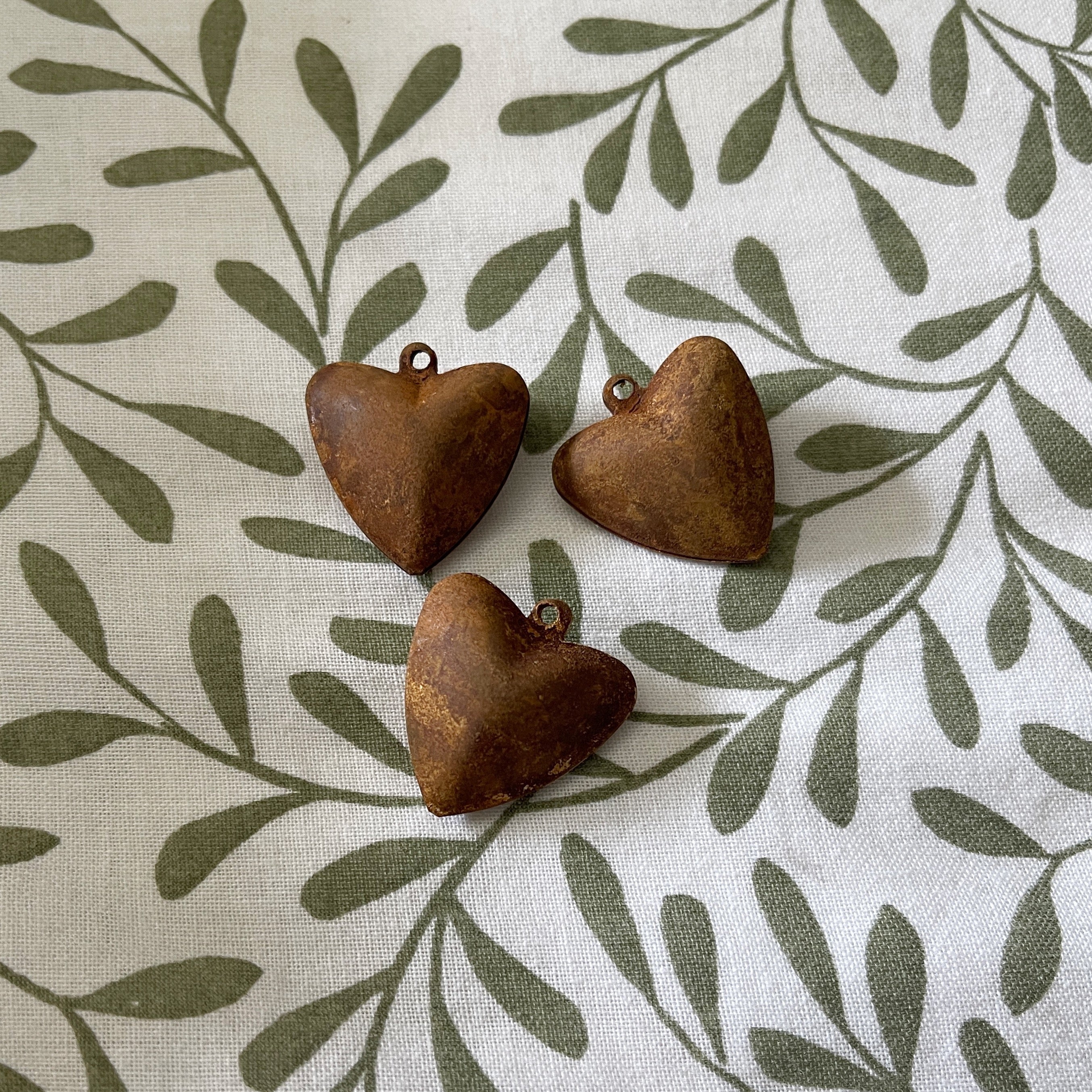 Three rusted heart-shaped objects on a fabric background with leaf pattern